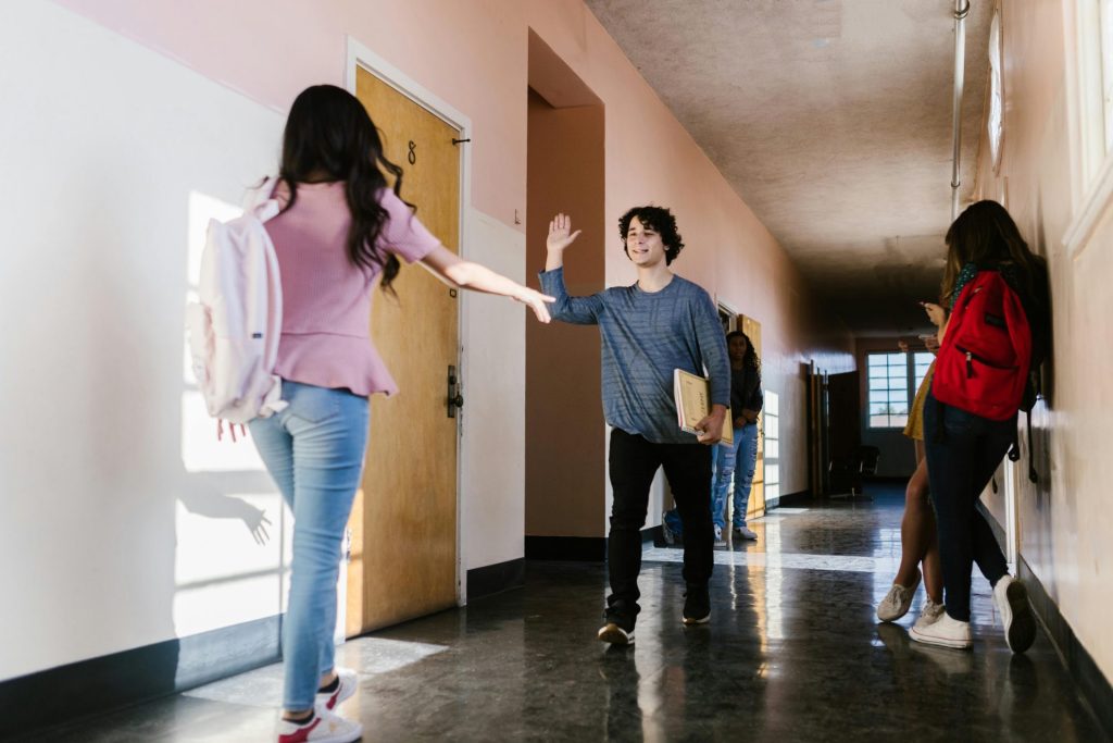 Teens greeting each other happily in a school hallway with natural light.