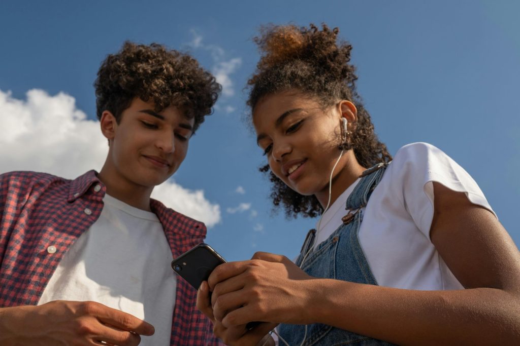 Two teenagers enjoy music together outdoors using a smartphone and earphones.